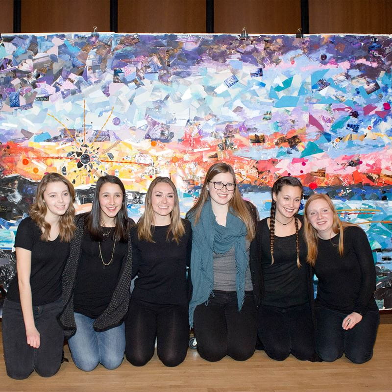 6 students kneeling in front of large art piece