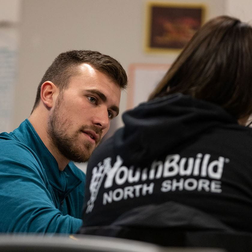 male intern teaching a student wearing a black "youth build north shore" tee shirt