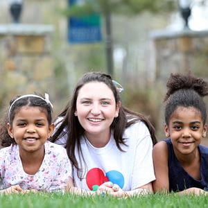 student laying in grass with two little girls